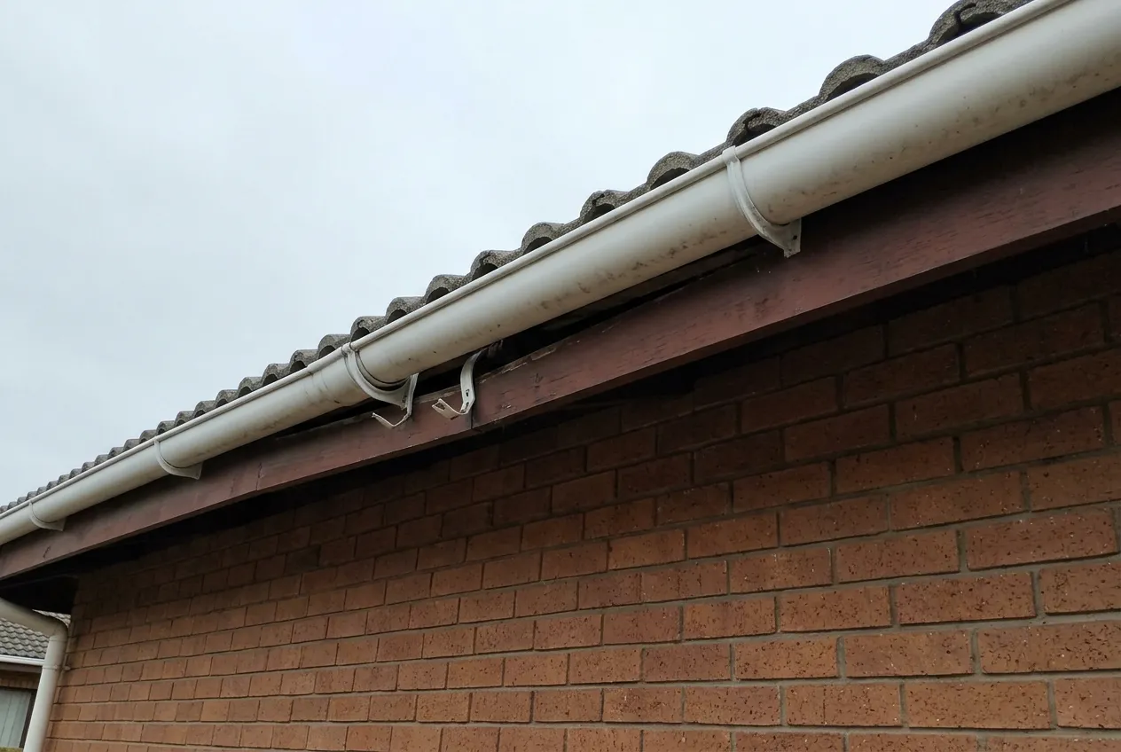 PVC gutter sagging away from the fascia board of a single-storey face-brick house where the brackets have pulled loose